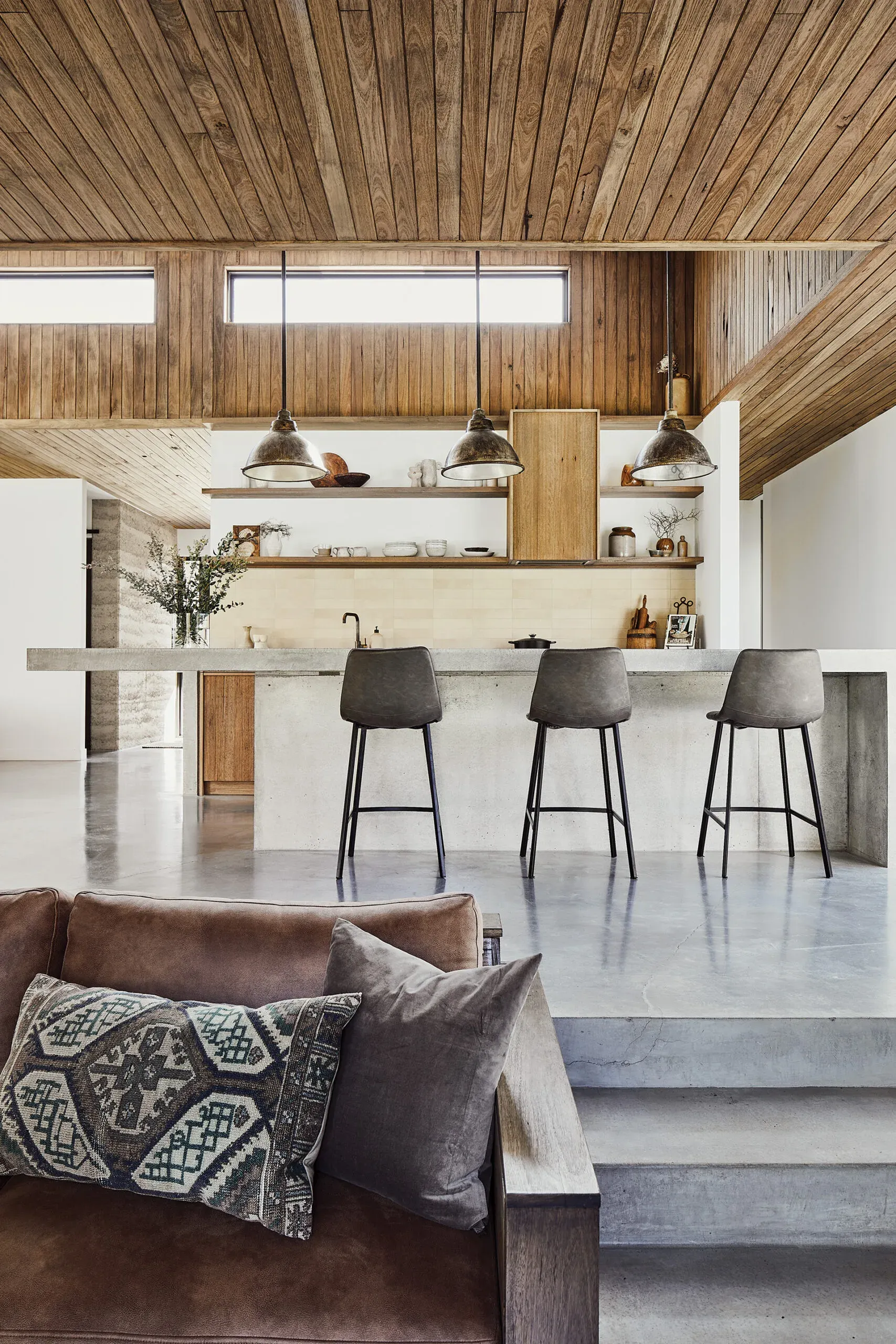 A poured concrete kitchen island and honed concrete floor under a timber cathedral ceiling
