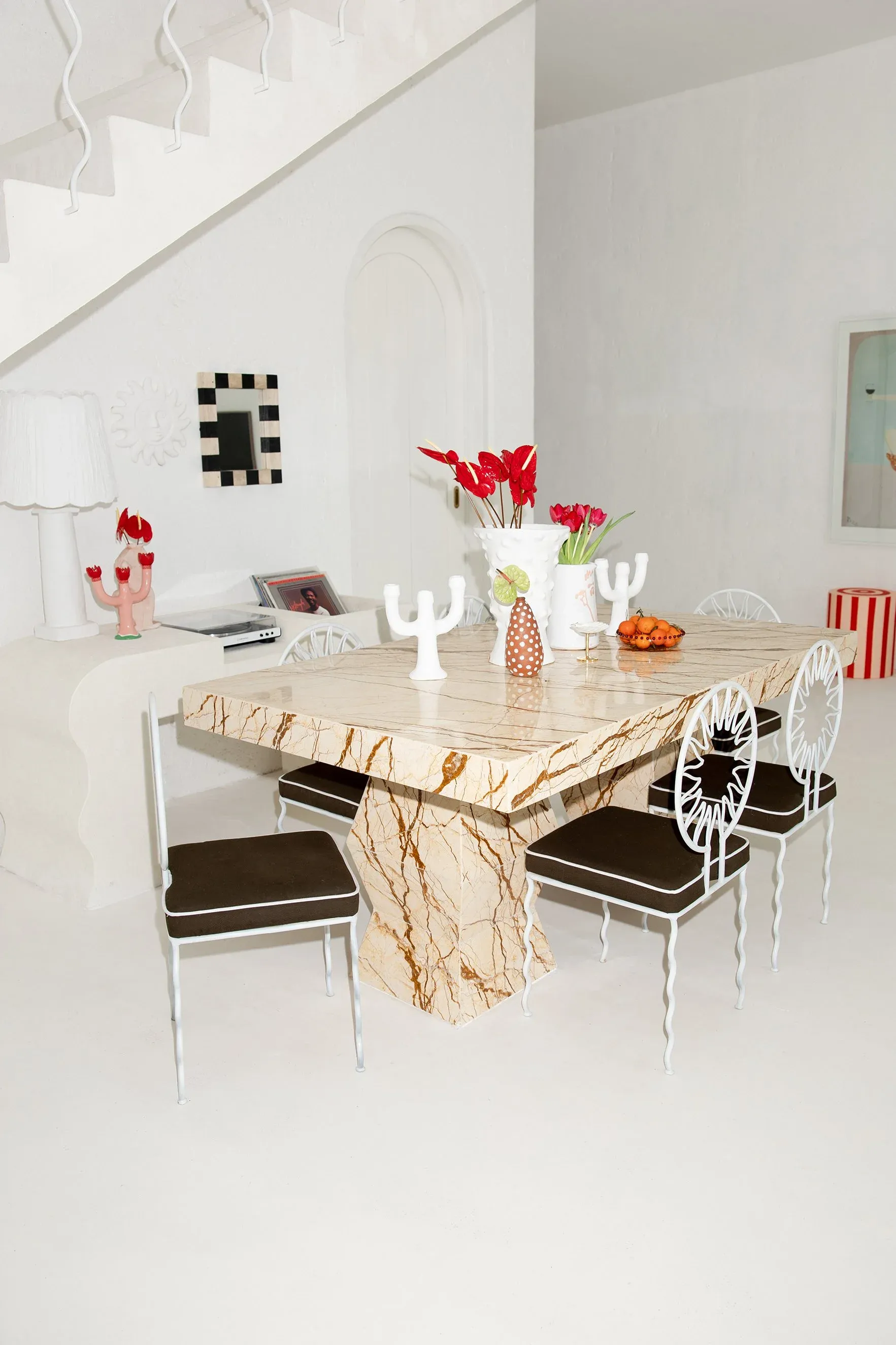 A white Mediterranean dining room with a marble table and white wire chairs on a poured white floor