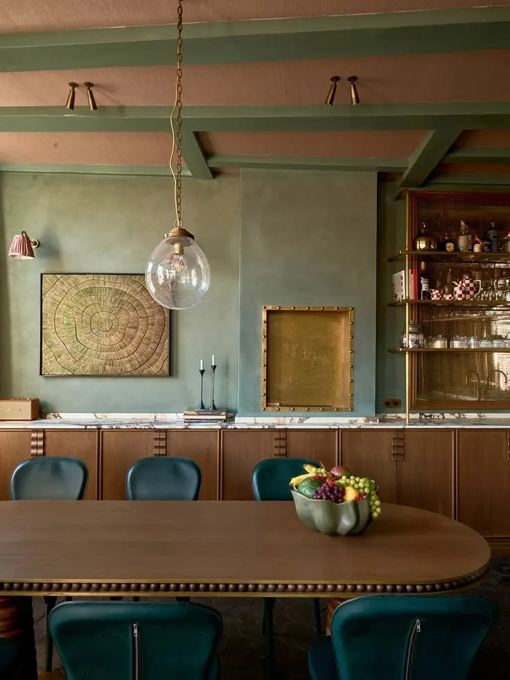 A dining room in deep sage limewash, chalky and matte, with brass and bottle-green chairs.